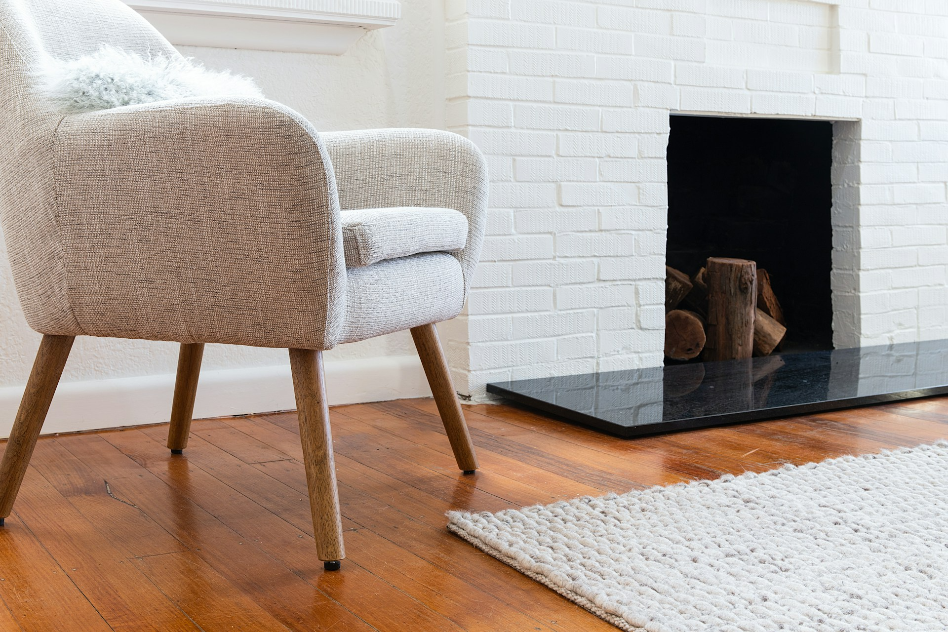 Professional cleaning of a textured wool area rug and woven armchair in a luxury Dartmouth property near a white brick fireplace.